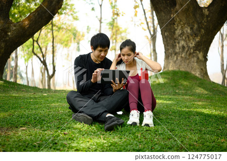 Sporty couple sitting on the grass in a peaceful park and using digital tablet 124775017