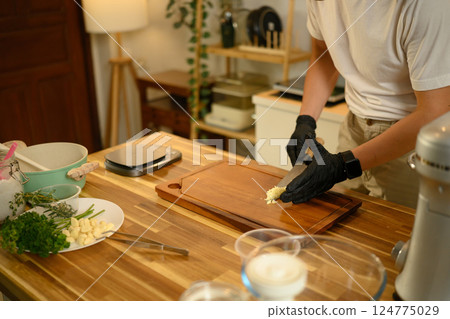 Close up of man chopping garlic on wooden cutting board in a modern kitchen 124775029