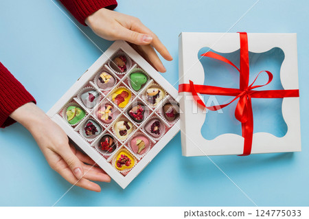 Female hands with delicious candies in box on color background 124775033