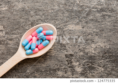 Vitamin capsules in a spoon on a colored background. Pills served as a healthy meal. Red soft gel vitamin supplement capsules on spoon 124775335