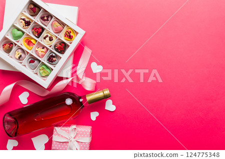 Bottle of red wine on colored background for Valentine Day with gift and chocolate. Heart shaped with gift box of chocolates top view with copy space Bottle of red wine on colored background for Valentine Day with gift and chocolate. Heart shaped with gift box of chocolates top view with copy space 124775348