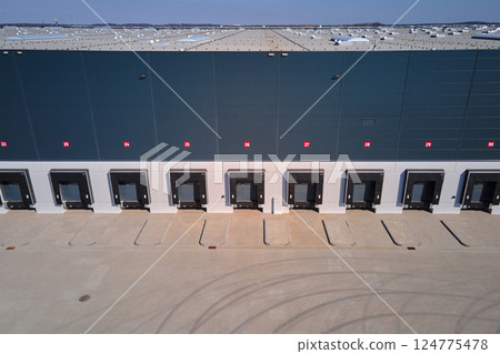 Aerial view of logistics warehouse exterior with loading platforms. Truck bays at distribution center with closed loading gates. Commercial infrastructure for freight operations 124775478