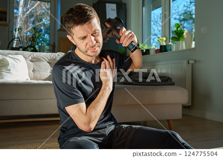 Man applies massage gun to relieve tension in neck and shoulder area. Male athlete doing self-massage therapy with percussion device for recovery after training Man applies massage gun to relieve tension in neck and shoulder area. Male athlete doing self-massage therapy with percussion device for recovery after training 124775504
