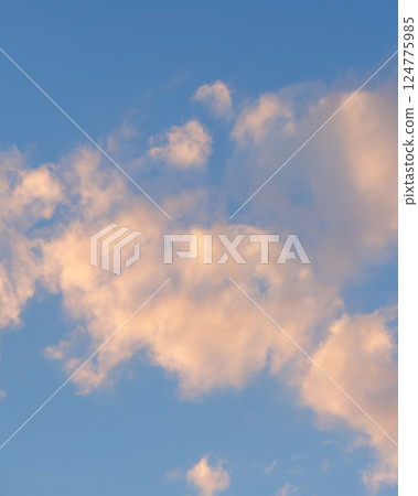 Soft pastel clouds illuminated by the warm evening sun against a clear blue sky Soft pastel clouds illuminated by the warm evening sun against a clear blue sky 124775985