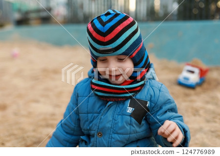 Child enjoying playtime in a sandbox at a park during a cool autumn afternoon while wearing a Child enjoying playtime in a sandbox at a park during a cool autumn afternoon while wearing a 124776989
