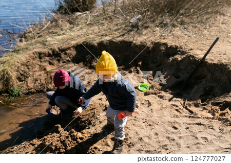 Children playing near the water on a sunny day, digging and exploring the sandy riverbank at a local 124777027