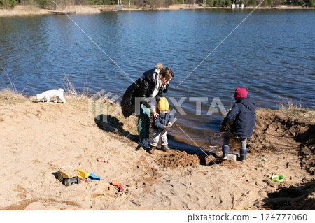 Children play in sand by the lake with an adult supervising on a sunny spring day 124777060