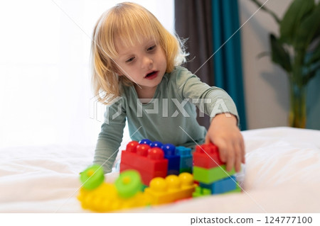 Child builds colorful structures with blocks on a bed in a cozy indoor setting during the afternoon Child builds colorful structures with blocks on a bed in a cozy indoor setting during the afternoon 124777100