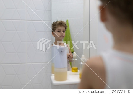 Young boy gazes thoughtfully at his reflection in bathroom mirror during morning routine Young boy gazes thoughtfully at his reflection in bathroom mirror during morning routine 124777168