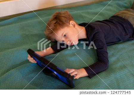Child enjoying tablet on a teal blanket at home during a quiet afternoon in autumn Child enjoying tablet on a teal blanket at home during a quiet afternoon in autumn 124777545