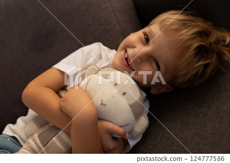 Smiling boy cuddling a stuffed animal on a couch during a cozy afternoon at home 124777586