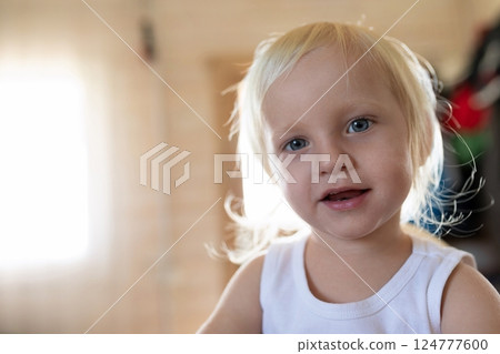 Child with light blonde hair smiling in a cozy indoor setting during daylight hours, capturing 124777600