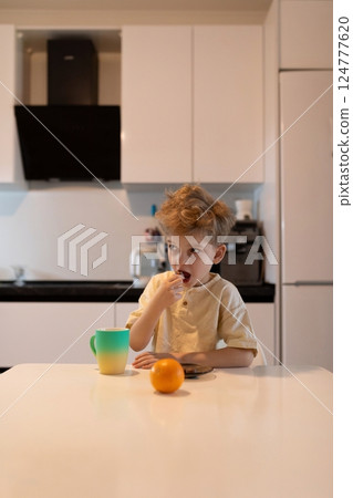 Young boy enjoys snack and drink at kitchen table in modern home during daytime Young boy enjoys snack and drink at kitchen table in modern home during daytime 124777620