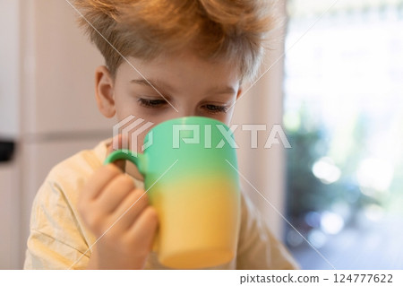 Young child enjoys a colorful mug of beverage while sitting at home in daytime Young child enjoys a colorful mug of beverage while sitting at home in daytime 124777622