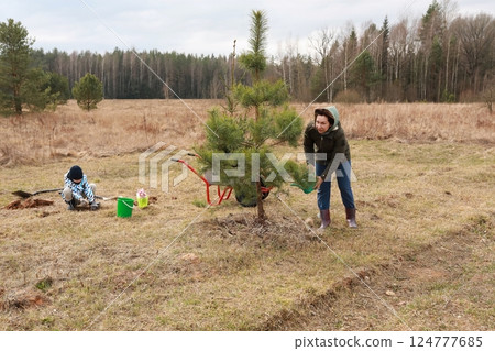 Community members planting trees in a wooded area during a cloudy day in early spring 124777685