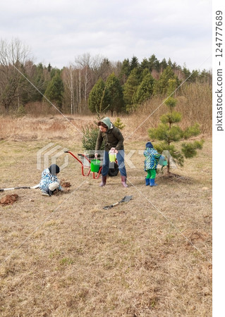 Family engages in tree planting activity in a rural field during springtime 124777689