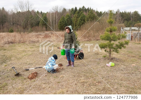 Mother and child planting a tree in a rural area during a cloudy afternoon Mother and child planting a tree in a rural area during a cloudy afternoon 124777986