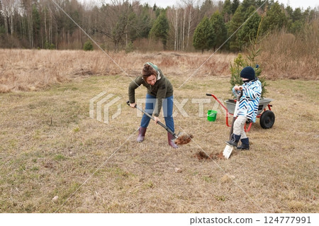 Family planting trees in a grassy field during a spring afternoon in a rural natural setting Family planting trees in a grassy field during a spring afternoon in a rural natural setting 124777991