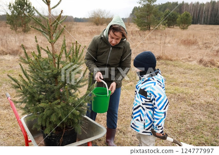Mother and child planting a tree in early spring at a rural field in nature Mother and child planting a tree in early spring at a rural field in nature 124777997
