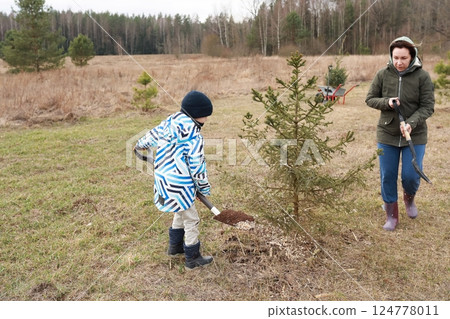 Child and adult plant a tree together in a natural setting during early spring in a rural area 124778011