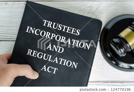 Hand holding Trustee Incorporation and Regulation Act book with gavel background Hand holding Trustee Incorporation and Regulation Act book with gavel background 124778196