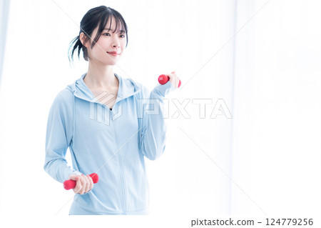 Young woman doing dumbbell training in a bright room 124779256
