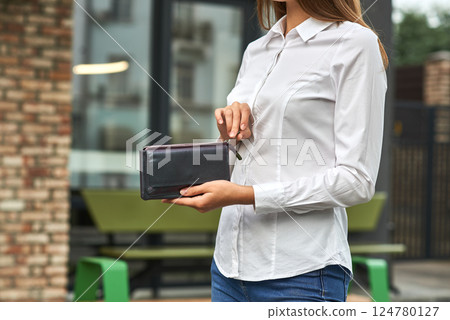 Woman in white shirt holding black leather wallet outdoors, focus on wallet, modern fashion accessory concept 124780127