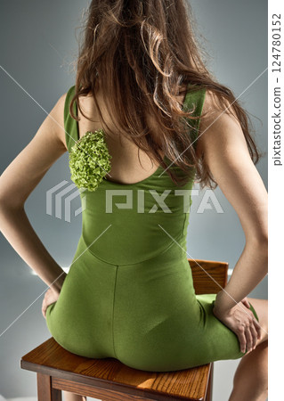 Elegant woman in green dress sitting on wooden stool with hydrangea flower on back, floral fashion concept Elegant woman in green dress sitting on wooden stool with hydrangea flower on back, floral fashion concept 124780152