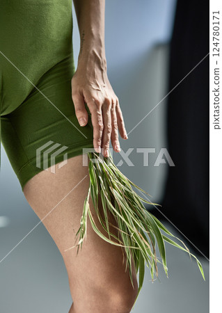 Person in green outfit with grass details touching leg gracefully, nature and fashion fusion concept 124780171