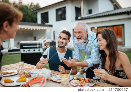 Older man showing photos on smartphone during spring family barbecue. 124780667