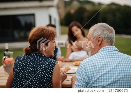 Family sitting at table and eating delicious food during spring family barbecue. 124780673