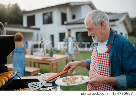Senior man grilling food for a spring family weekend barbecue. 124780697