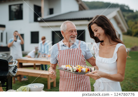 Older father and adult daughter preparing food for a family barbecue. 124780776