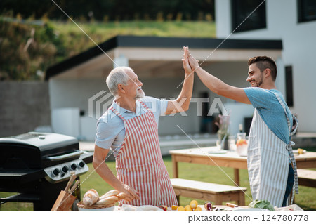 Father-in-law and son-in-law preparing food for a family barbecue. 124780778