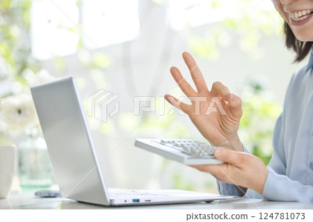 一位中年婦女在客廳一邊使用計算機一邊看著電腦 124781073