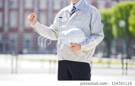 A young man in work clothes holding a helmet and making a fist pump 124781119