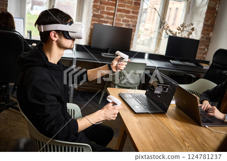 Man using virtual reality headset with controllers in modern office, technology and innovation in work environment concept Man using virtual reality headset with controllers in modern office, technology and innovation in work environment concept 124781237