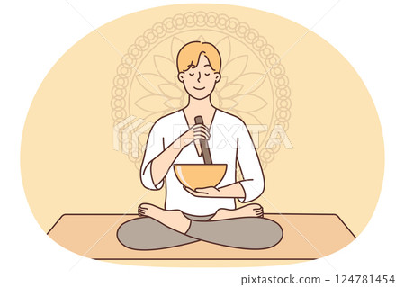 Meditating man sitting in lotus position on yoga mat using bowl to perform ancient ritual 124781454