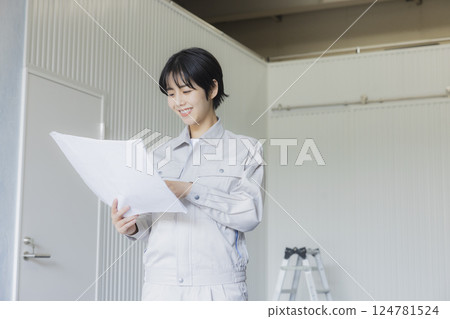 A woman in work clothes looking at a drawing in a factory A woman in work clothes looking at a drawing in a factory 124781524