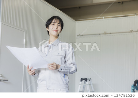 A woman in work clothes looking at a drawing in a factory A woman in work clothes looking at a drawing in a factory 124781526