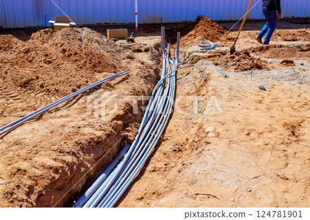 Workers organize electrical conduits in trench at construction site during foundation work 124781901