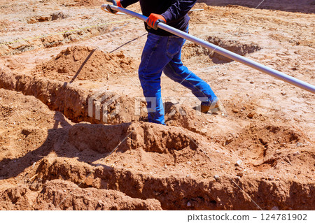 Worker laying out electrical pipes to shape sandy ground during foundation work 124781902