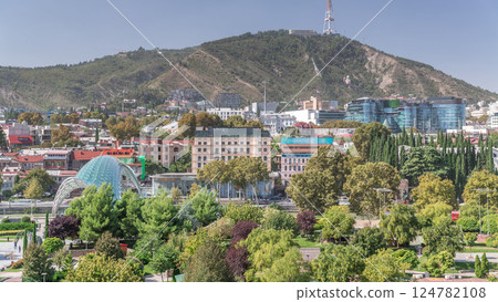 Aerial timelapse of Rike Park, a modern urban park in Tbilisi's Old Town with green trees and lawns. The Bridge of Peace in the background. Georgia Aerial timelapse of Rike Park, a modern urban park in Tbilisi's Old Town with green trees and lawns. The Bridge of Peace in the background. Georgia 124782108