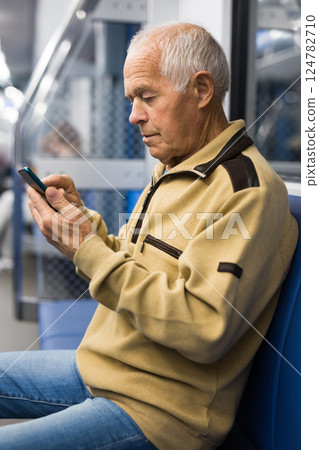 Old man sitting in subway car with smartphone 124782710