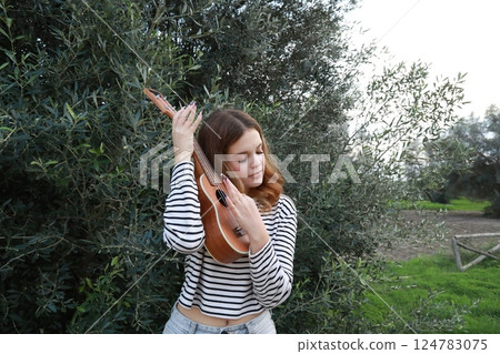 Artist Girl Plays Ukulele Musical Instrument Outside In Park Near A Tree 124783075