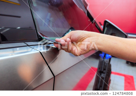 Worker carefully applies protective film to car window while working in an auto detailing shop Worker carefully applies protective film to car window while working in an auto detailing shop 124784808