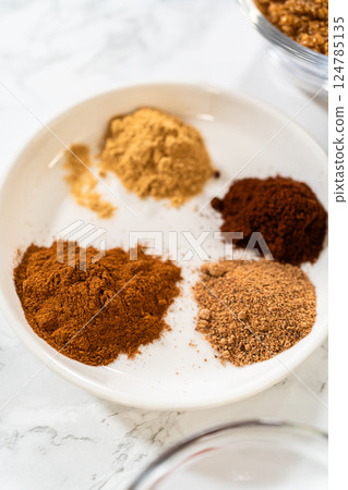 A white bowl containing the aromatic spices for Chocolate Gingerbread Cookie Dough, including cinnamon, ground ginger, cloves, and cocoa powder. These spices will infuse the dough with warm and rich A white bowl containing the aromatic spices for Chocolate Gingerbread Cookie Dough, including cinnamon, ground ginger, cloves, and cocoa powder. These spices will infuse the dough with warm and rich 124785135