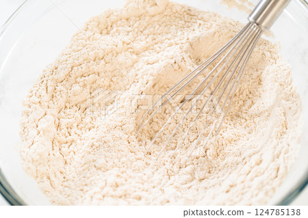 Close-up view of flour being whisked in a glass bowl, part of the initial steps in preparing Classic Gingerbread Cookie Dough. The whisk helps to evenly mix the dry ingredients before combining with Close-up view of flour being whisked in a glass bowl, part of the initial steps in preparing Classic Gingerbread Cookie Dough. The whisk helps to evenly mix the dry ingredients before combining with 124785138