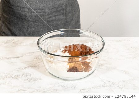 A bowl containing dry ingredients for Chocolate Gingerbread Cookie Dough, including cocoa powder, spices, and flour, ready to be mixed on a marble countertop. 124785144