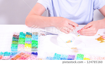 Delicate fingers of a young girl navigate through a treasure trove of bright, multicolored beads, each compartment revealing a new hue to choose from. Delicate fingers of a young girl navigate through a treasure trove of bright, multicolored beads, each compartment revealing a new hue to choose from. 124785160